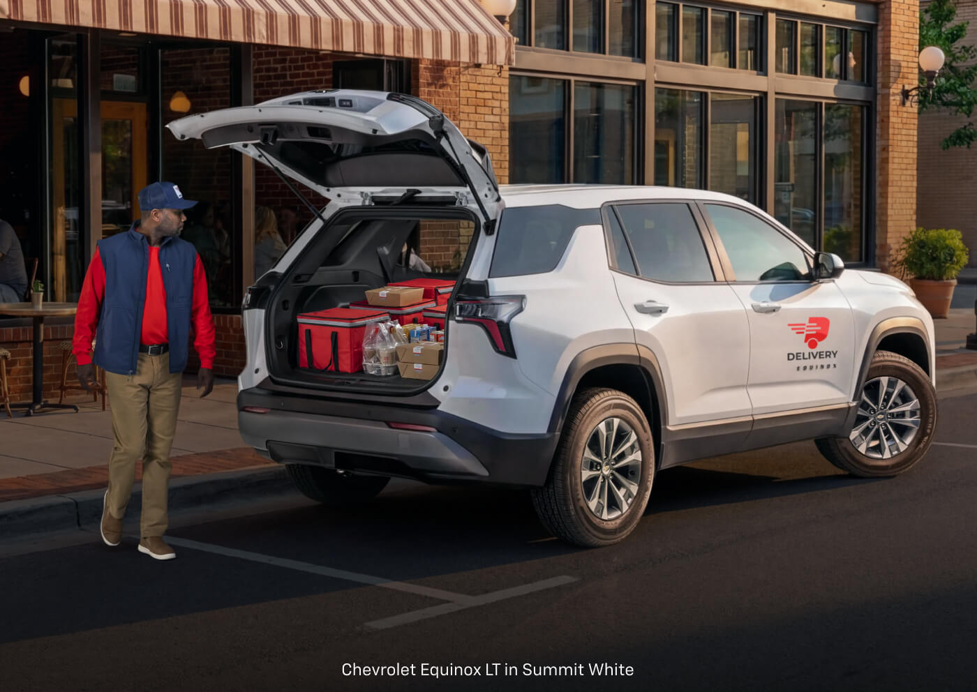 Rear three-quarter view of a Chevrolet Equinox LT in White with a delivery worker walking by.
