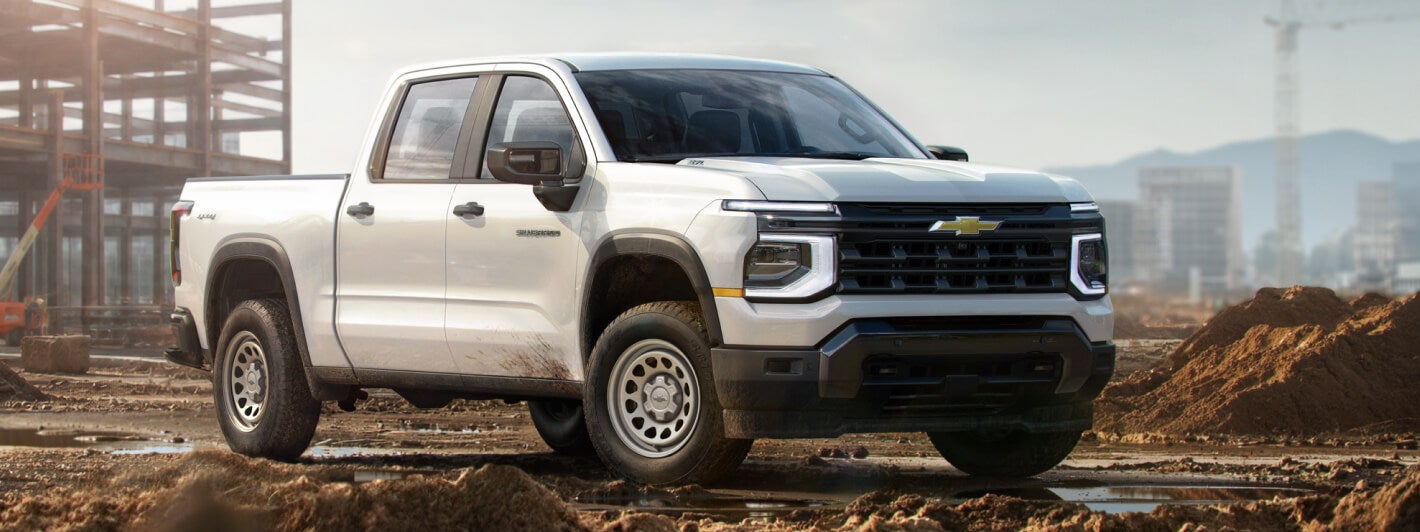 Three-quarter side view of a white 2027 Chevy Silverado 1500 Work Truck parked on a construction site.