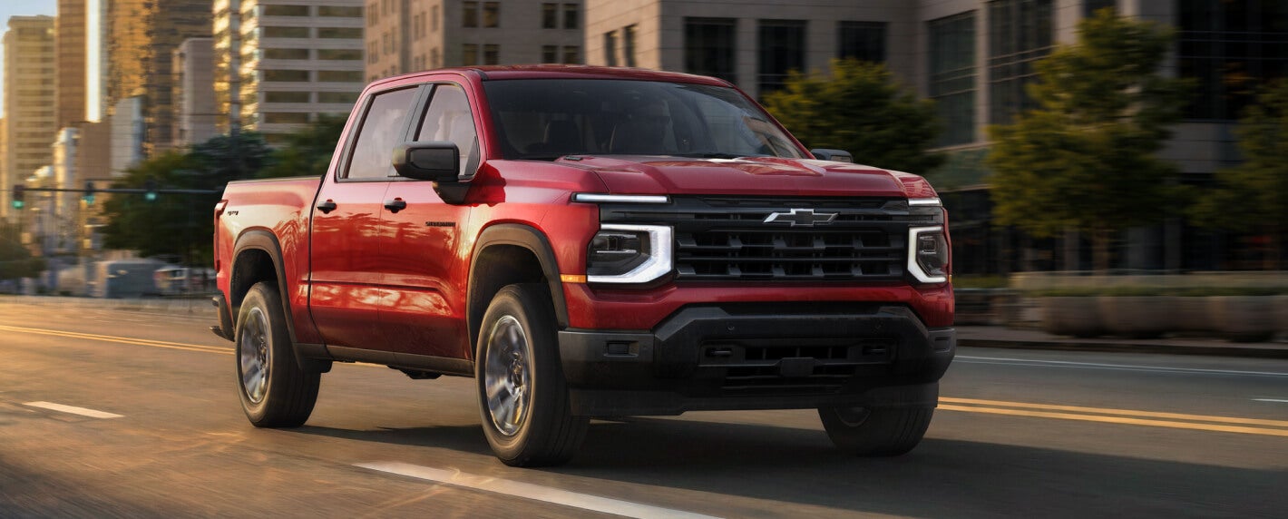 Three-quarter view of a red 2027 Chevy Silverado Custom driving on a city street.