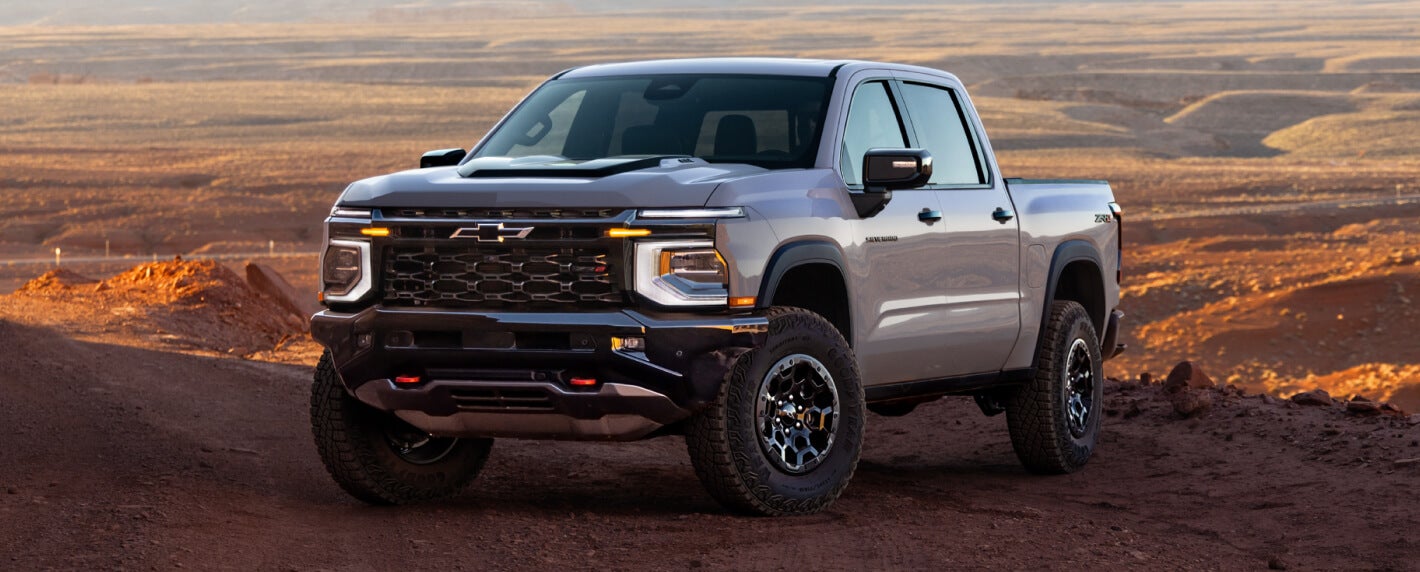 Exterior view of a silver 2027 Chevy Silverado ZR2 parked offroad on a scenic desert vista at dusk.