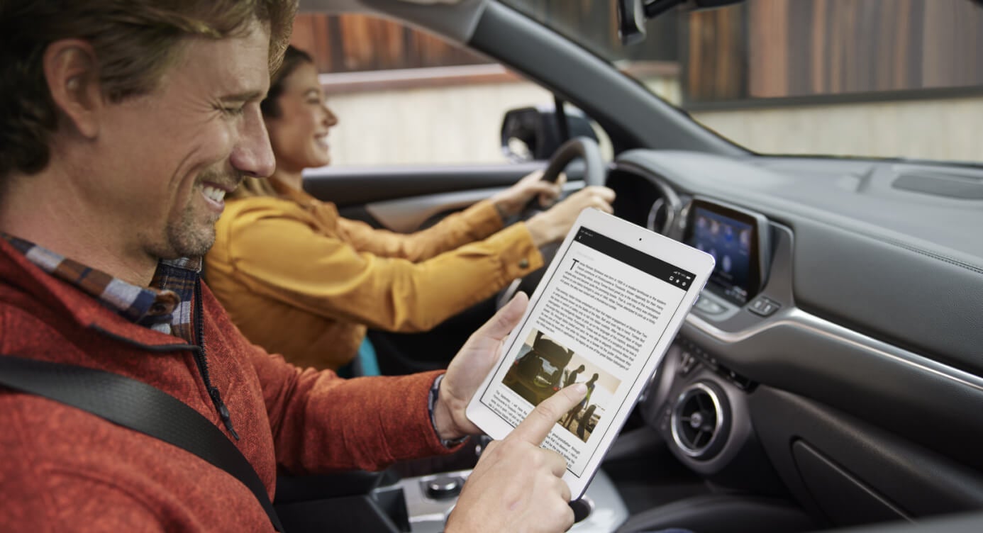 Interior view of a front passenger using a digital tablet while a woman drives a Chevrolet Blazer.
