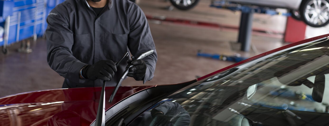 Close-up service view of a technician installing a new windshield wiper blade on a red Chevrolet Blazer.