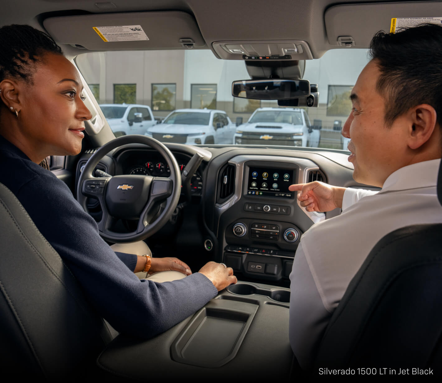 Two people sitting in the driver and passenger seat in the Chevrolet Silverado 1500 LT in Jet Black