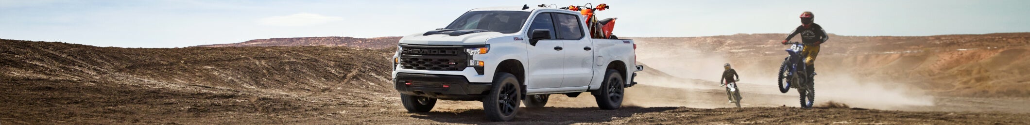 White Chevrolet pickup truck with dirt bikes in desert terrain