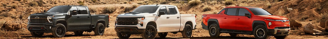Three Chevrolet pickup trucks in black, white, and red on desert terrain