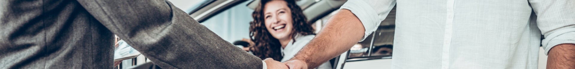 Men shake hands while woman smiles in the background, a proud new Chevy owner