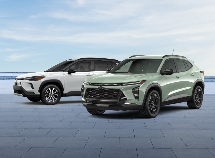 A green Chevy Trax and a white Toyota Corolla Cross parked in a bright concrete lot on a bright sunny day.