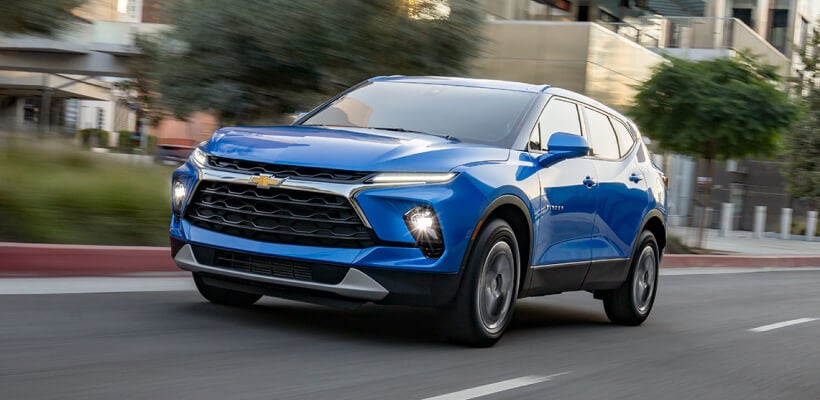 Front three-quarter view of blue Chevrolet Blazer driving on a city street near buildings.